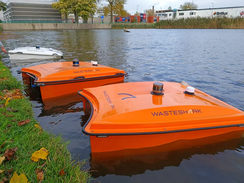 Two orange WasteShark vessels moored at a grassy canal bank